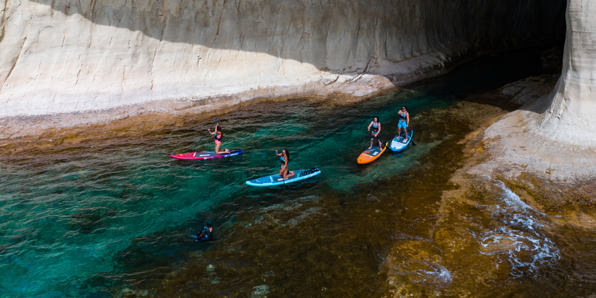 four people paddleboarding next to cliffs