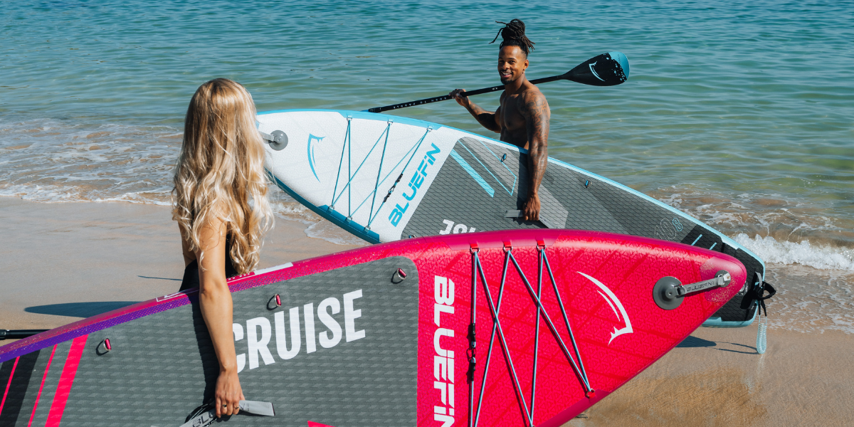 two people holding onto paddleboards looking towards each other with the beach in the background