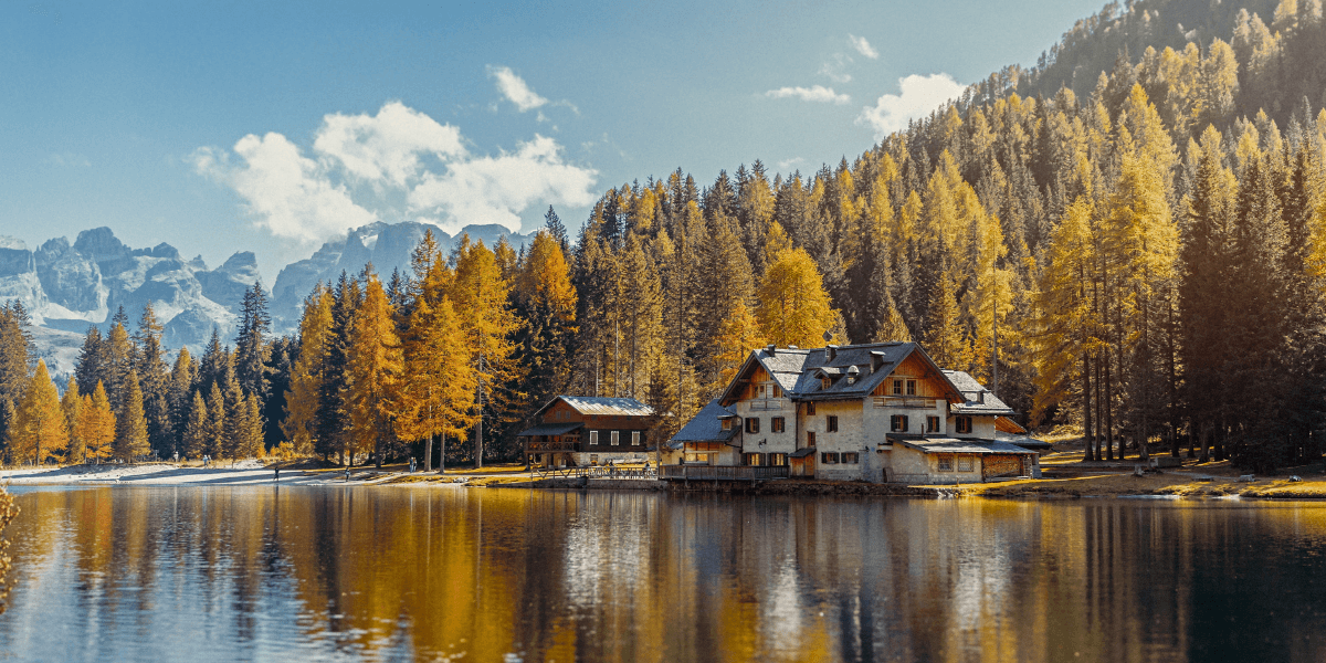 Autumn mountain lake with golden forest, alpine chalet and snowy peaks reflected in calm water