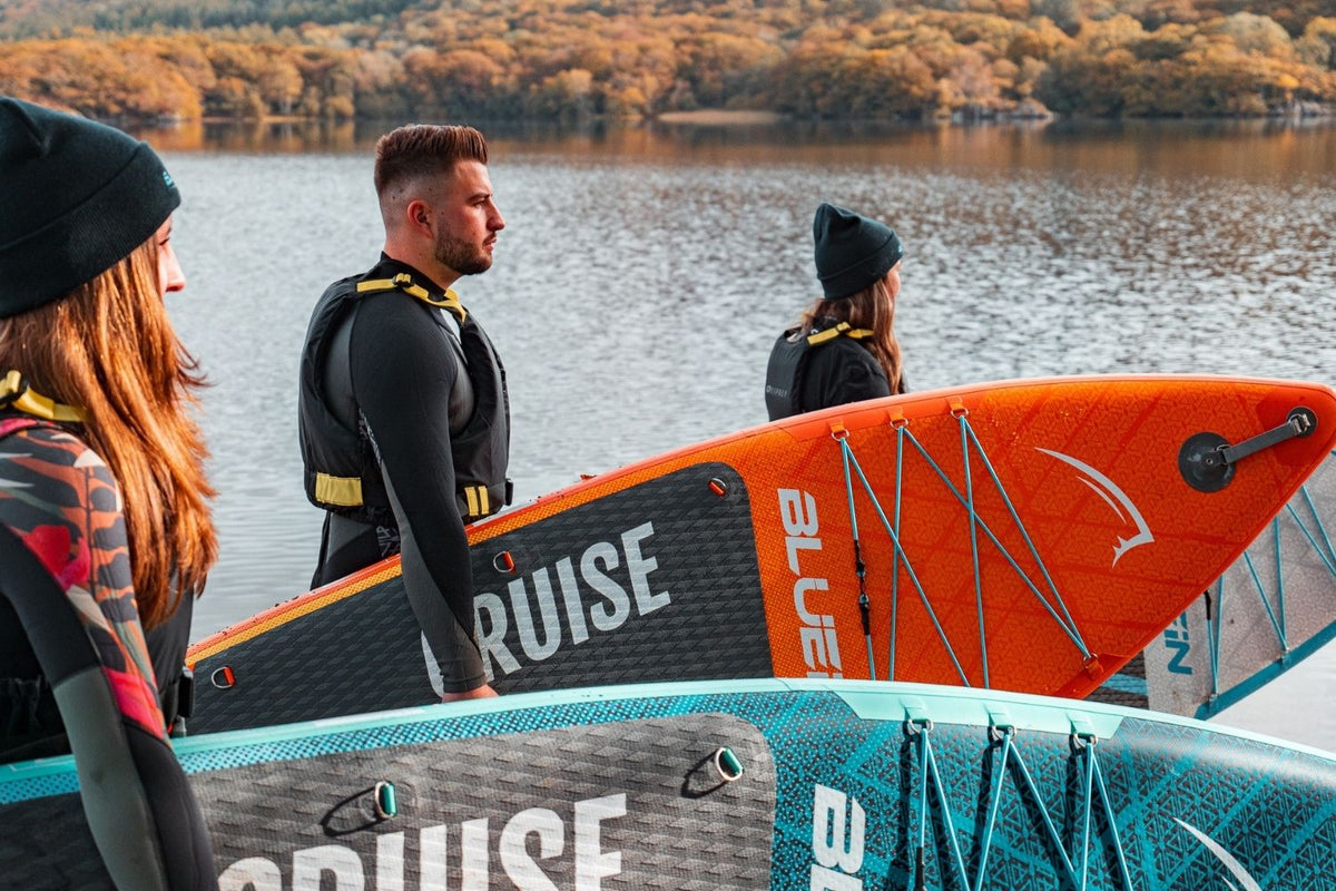 three people stood by a lake with autumn leaves in the foreground