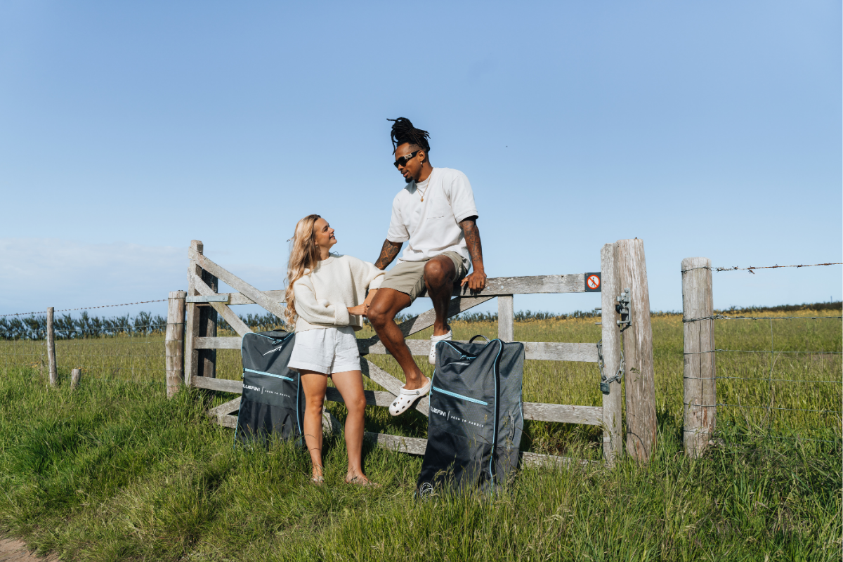 two people sat next to paddleboarding bags in a field