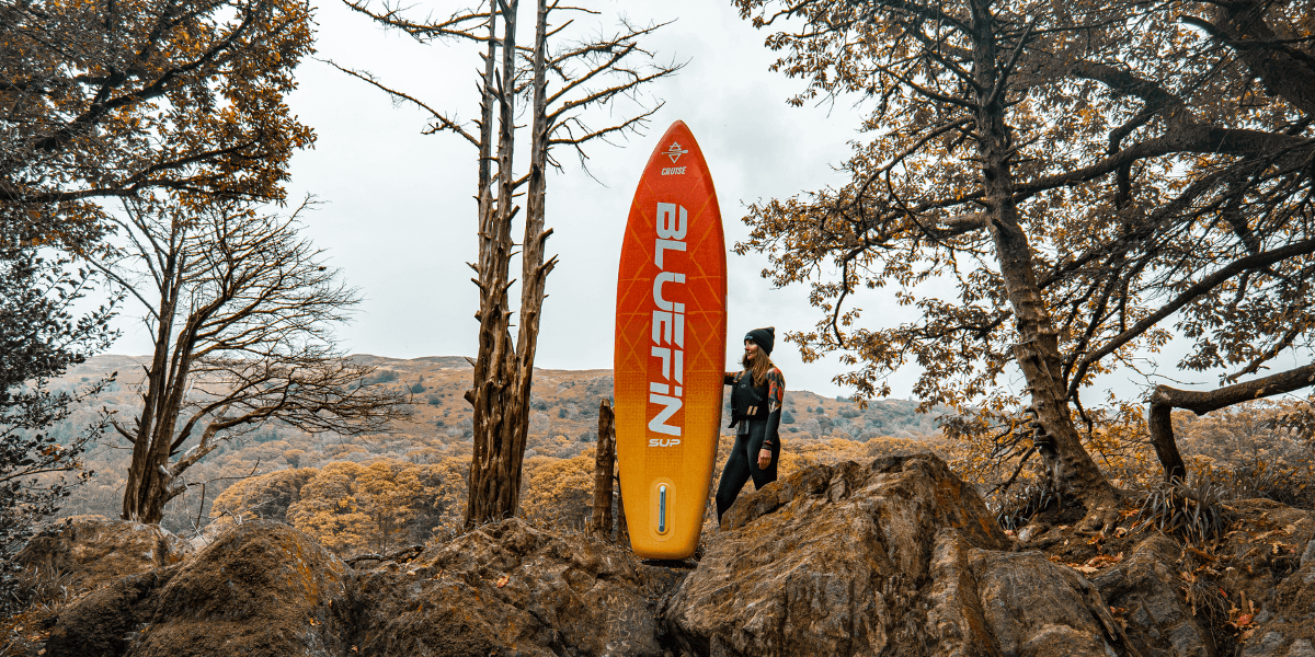 woman holding a paddleboard surrounded by autumn leaves