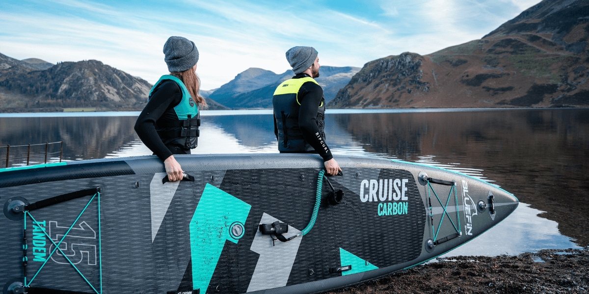 two people hoding a cruise carbon paddleboard looking out onto a lake