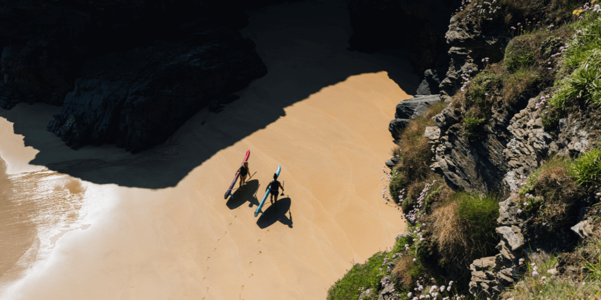 Two people walking down the beach with their Paddleboards