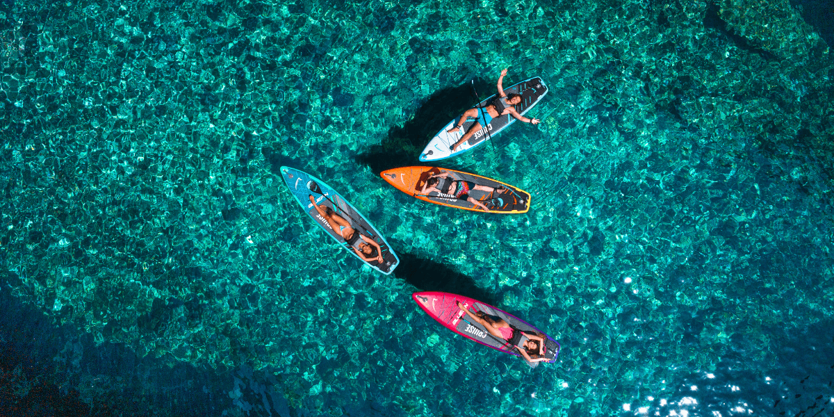 Aerial view of four people on colourful stand-up paddleboards in clear turquoise water