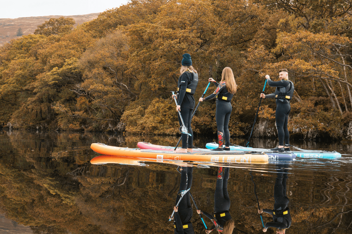three people paddleboarding on a lake with autumn leaves