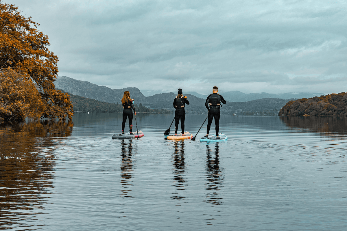 three people paddleboarding on a lake in autumn