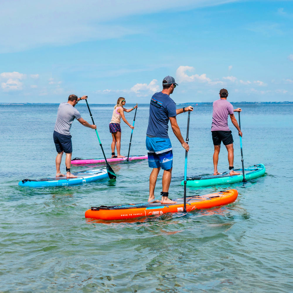 Four people paddleboarding on calm water under a blue sky.
