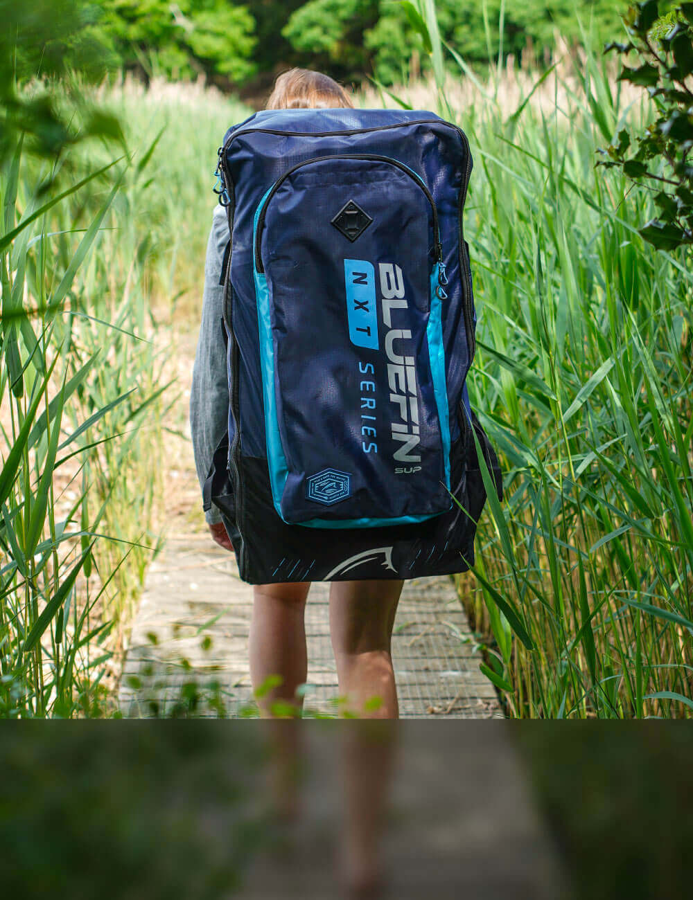 Girl walking through tall grass wearing a Bluefin backpack inflatable paddle board
