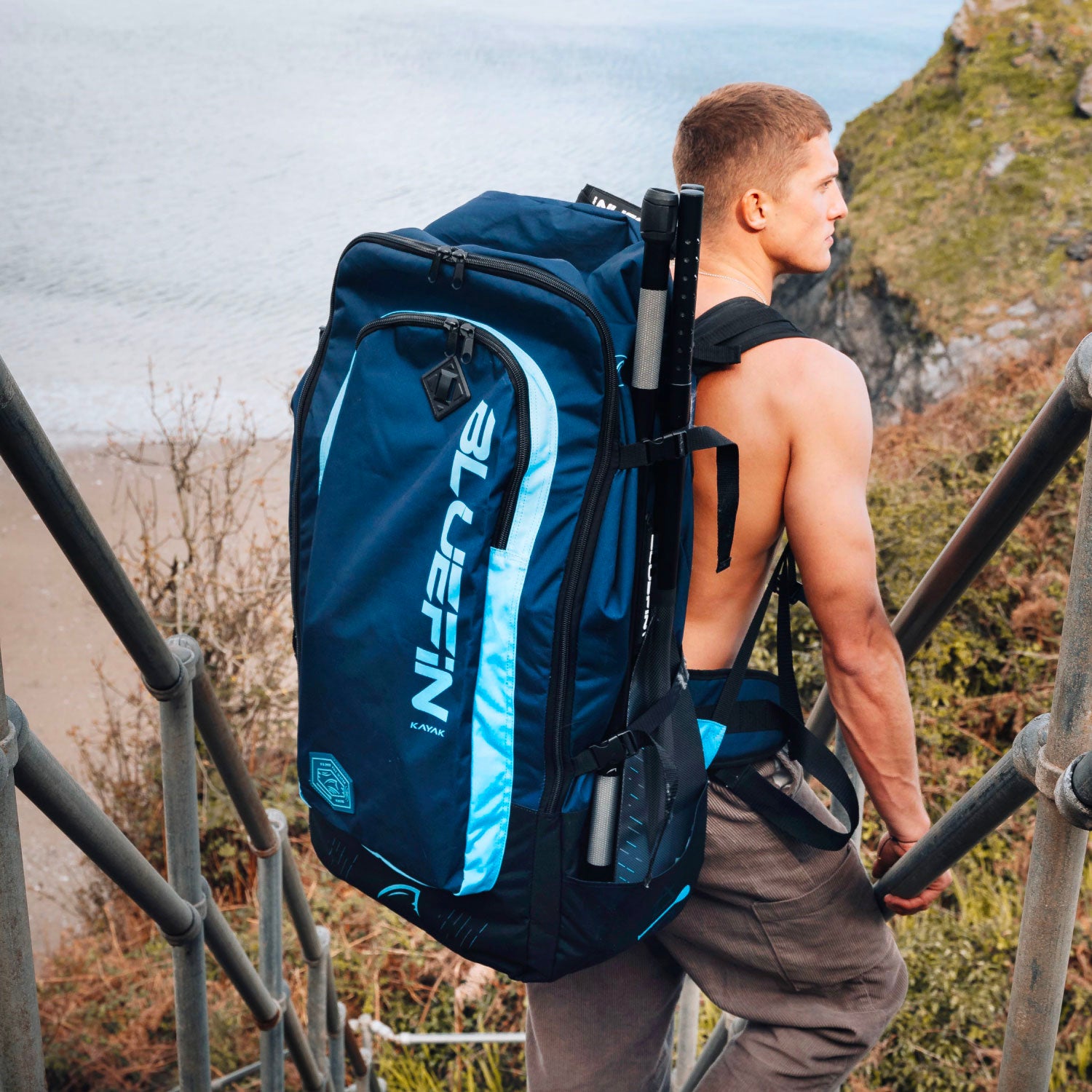 Man carrying a Bluefin SUP backpack while climbing stairs near the water.