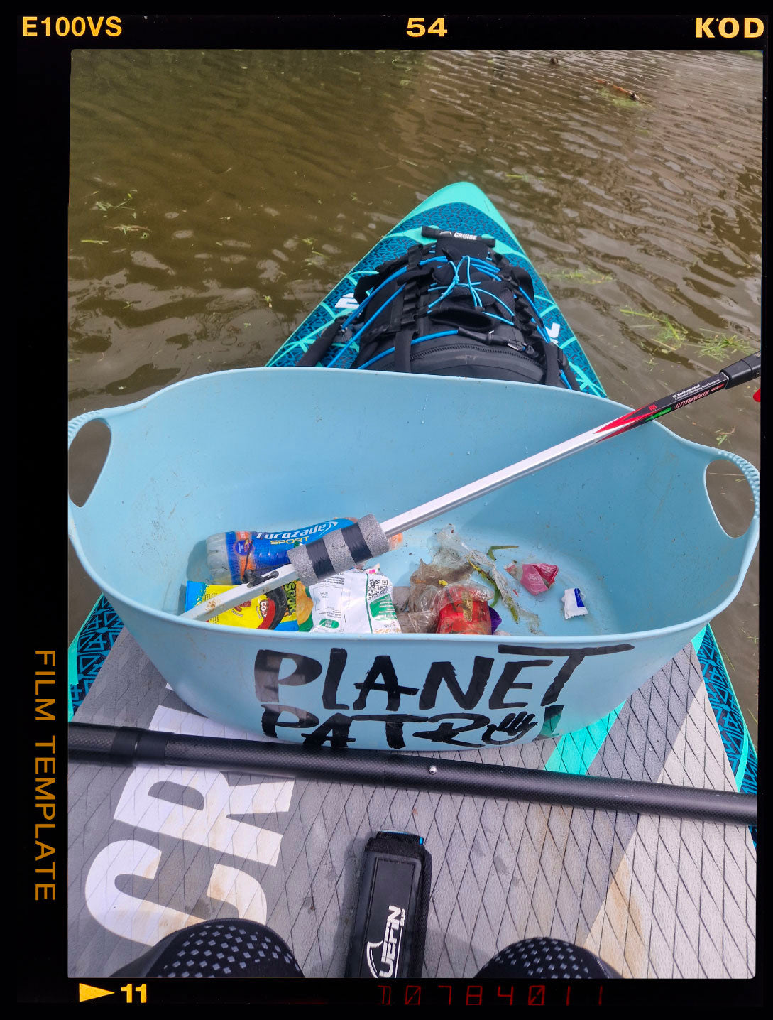 A paddleboarder collects trash in a blue bin labeled "Planet Patrol," floating on water.