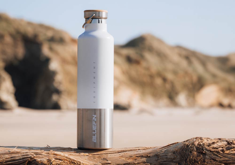 Bluefin insulated water bottle on a beach log with a blurred natural background.
