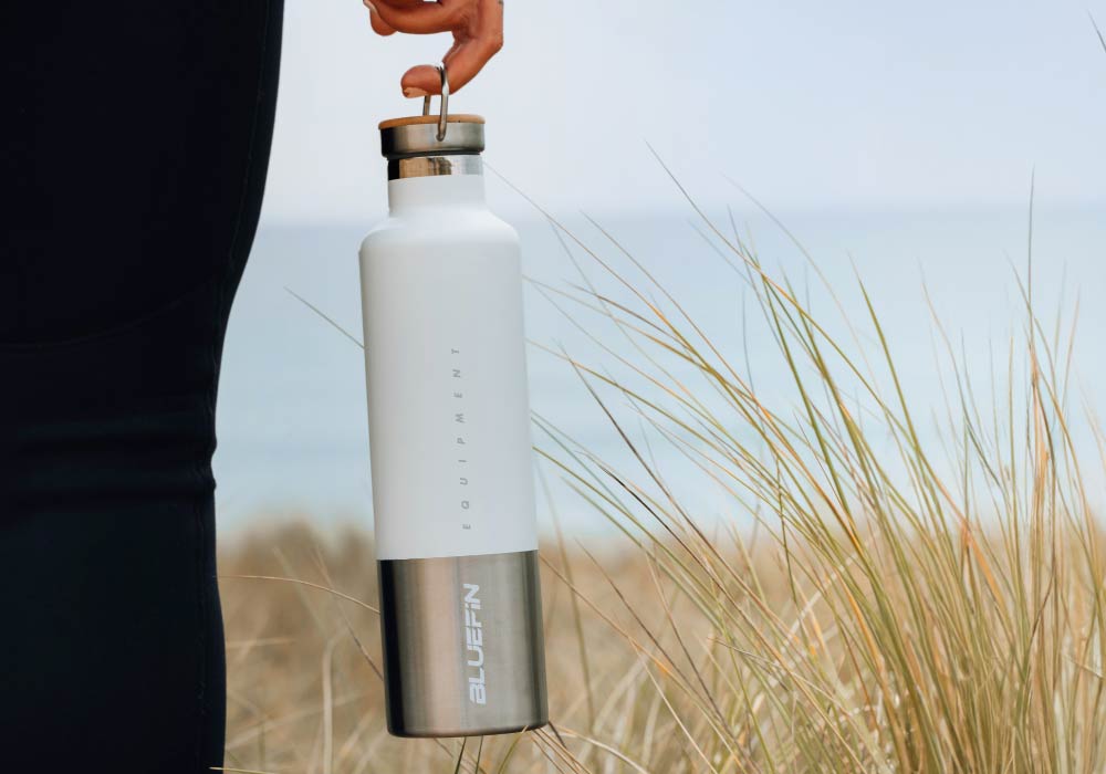 Person holding a stylish Bluefin water bottle against a beach backdrop with grass.