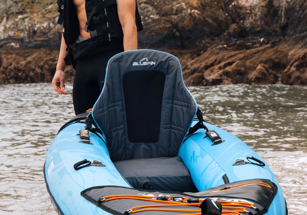Inflatable blue kayak with a comfortable seat, set against a rocky shoreline.