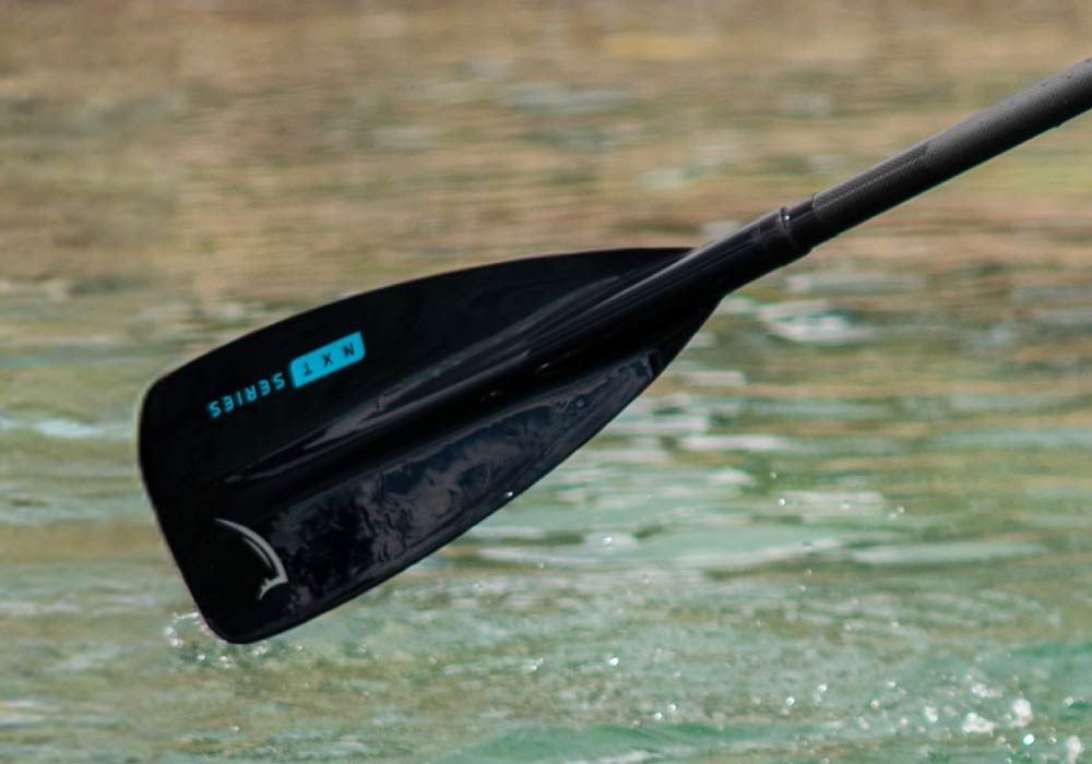 Black paddle from the NXt series, partially submerged in calm water, showcasing sleek design and functionality.