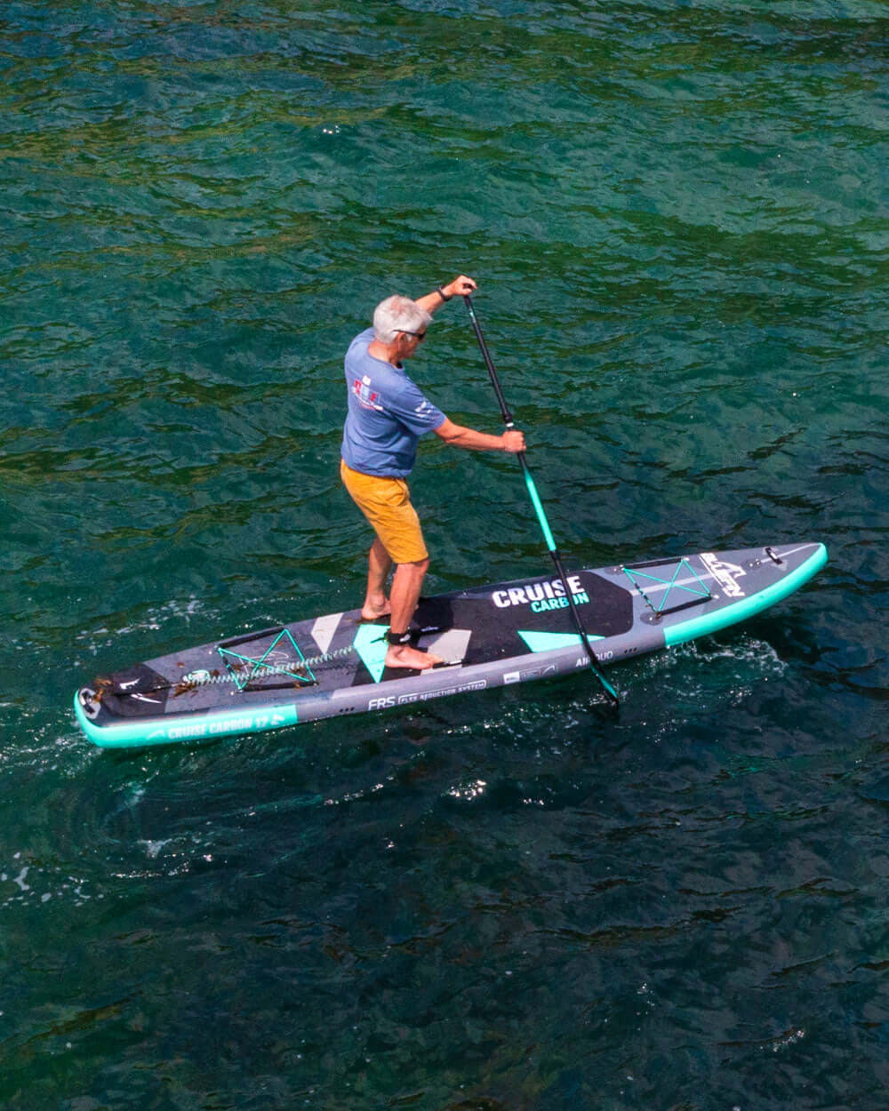 Man paddleboarding on a green and black Cruise Carbon paddle board with 'Cruise' branding in the ocean.