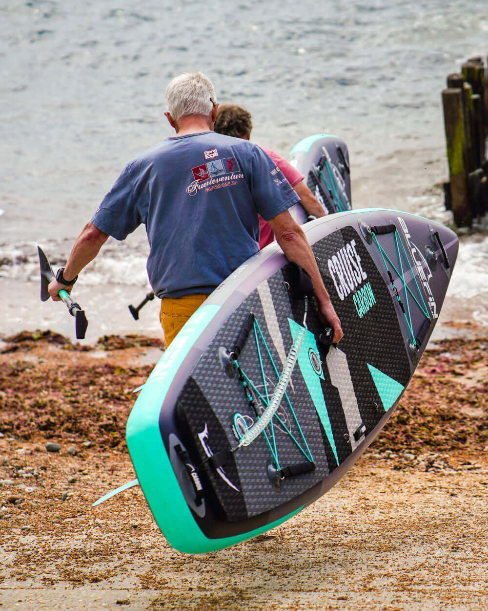 Two people carrying a Cruise carbon inflatable stand up paddle board