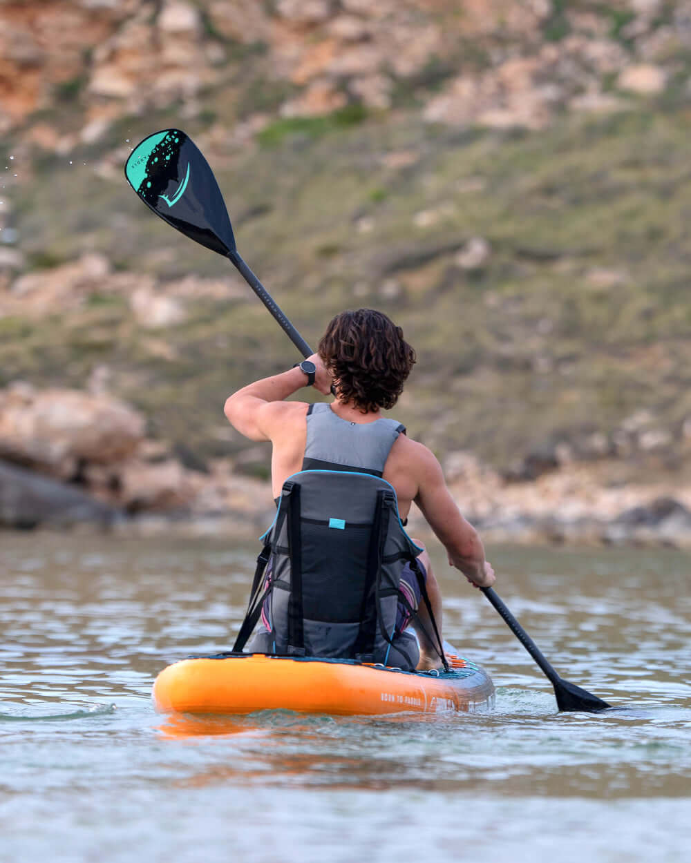 Paddler on an orange stand-up paddleboard navigating calm waters with a scenic background.
