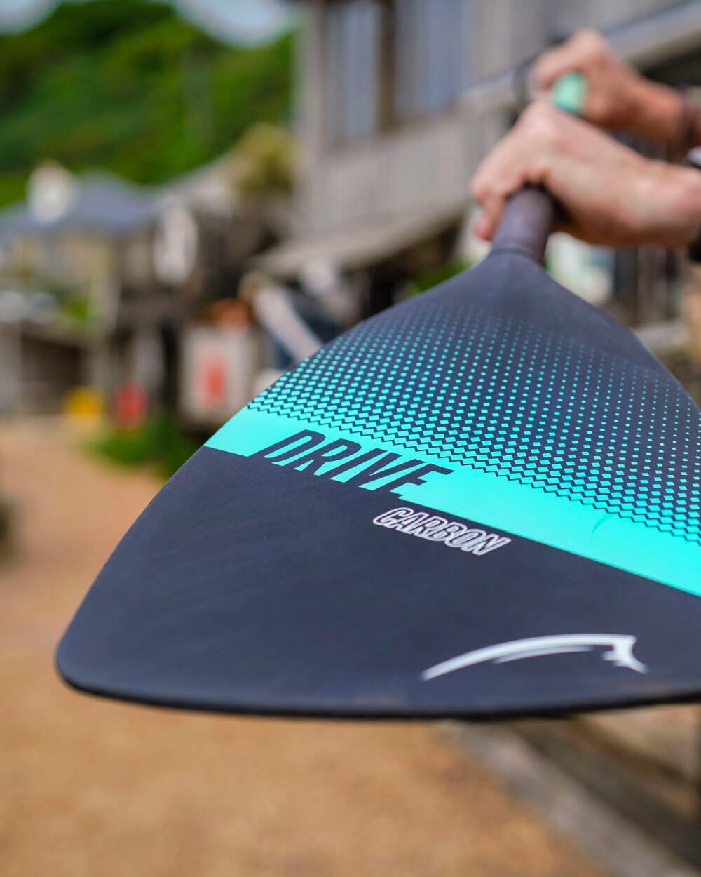 Close-up of a paddle with 'Drive Carbon' logo, held by a person outdoors.