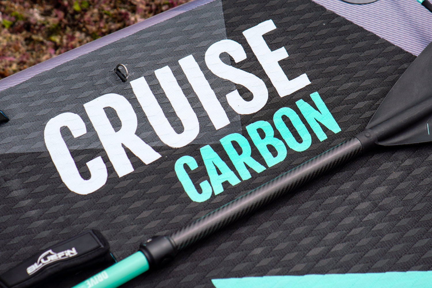 Close-up of a paddle board featuring the words "Cruise Carbon" and a carbon paddle.