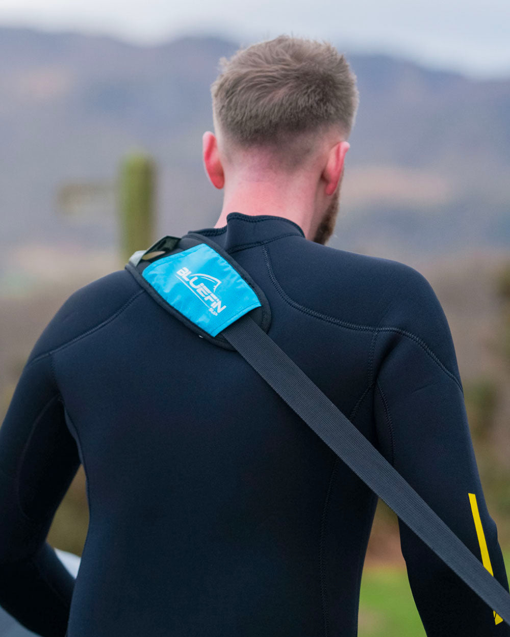 Person wearing a black wetsuit with a bluefin sup carry strap
