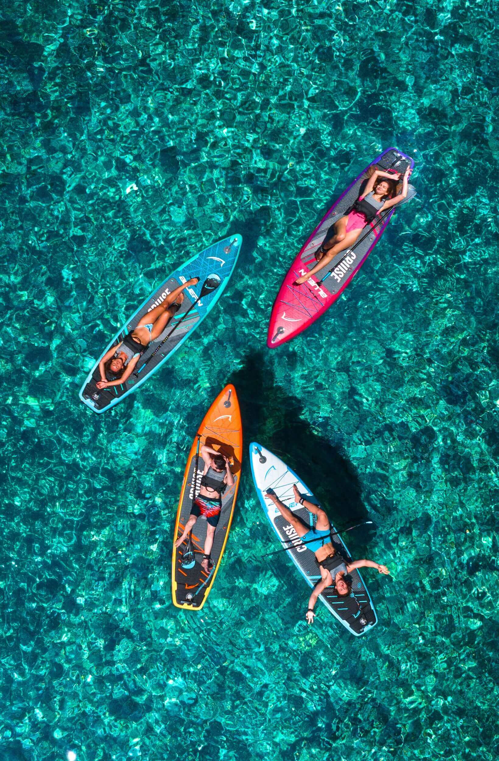 Four paddleboarders on colorful boards in clear water, enjoying a sunny day on the water.