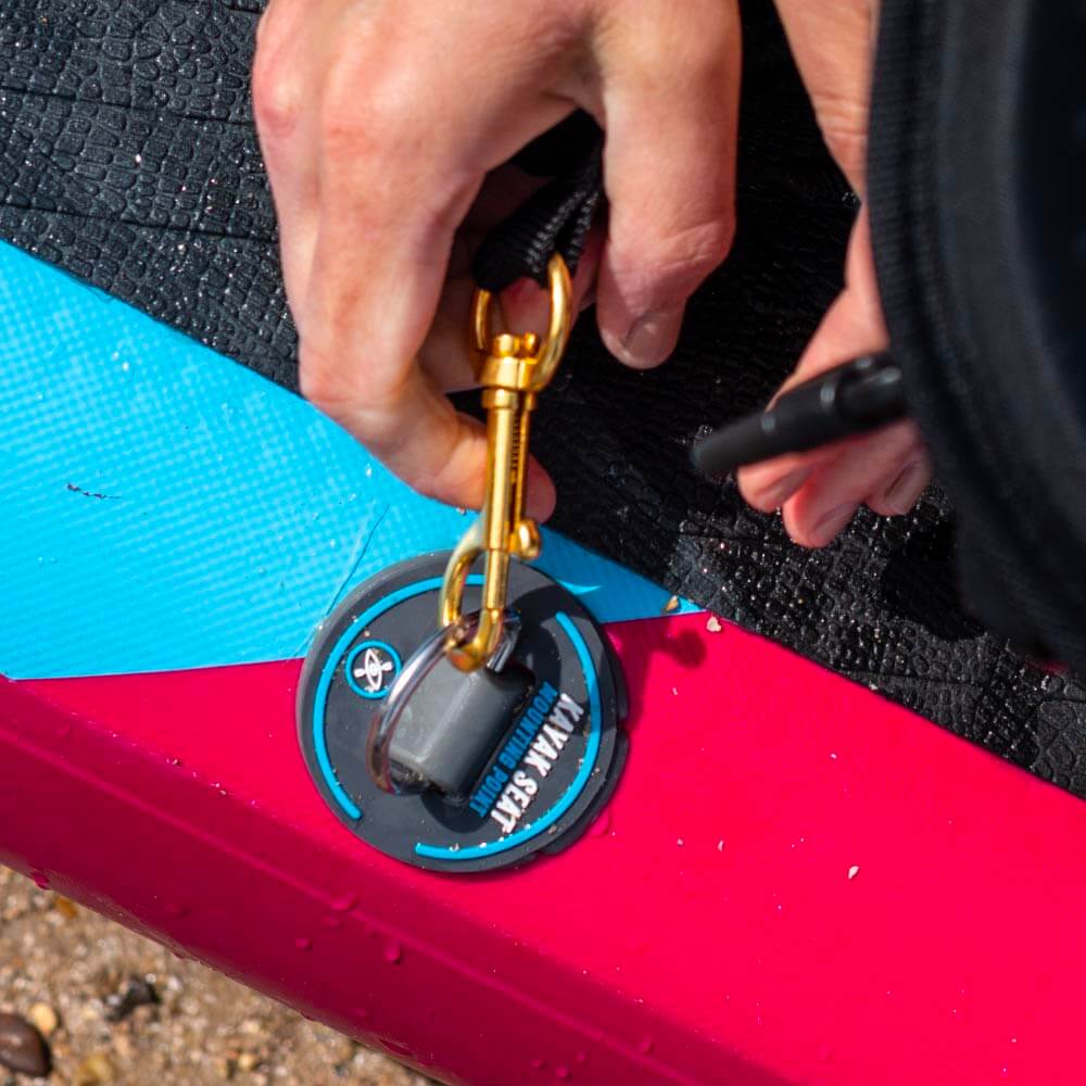 Hand securing a gold clip to a waterproof pad on a colorful paddleboard.