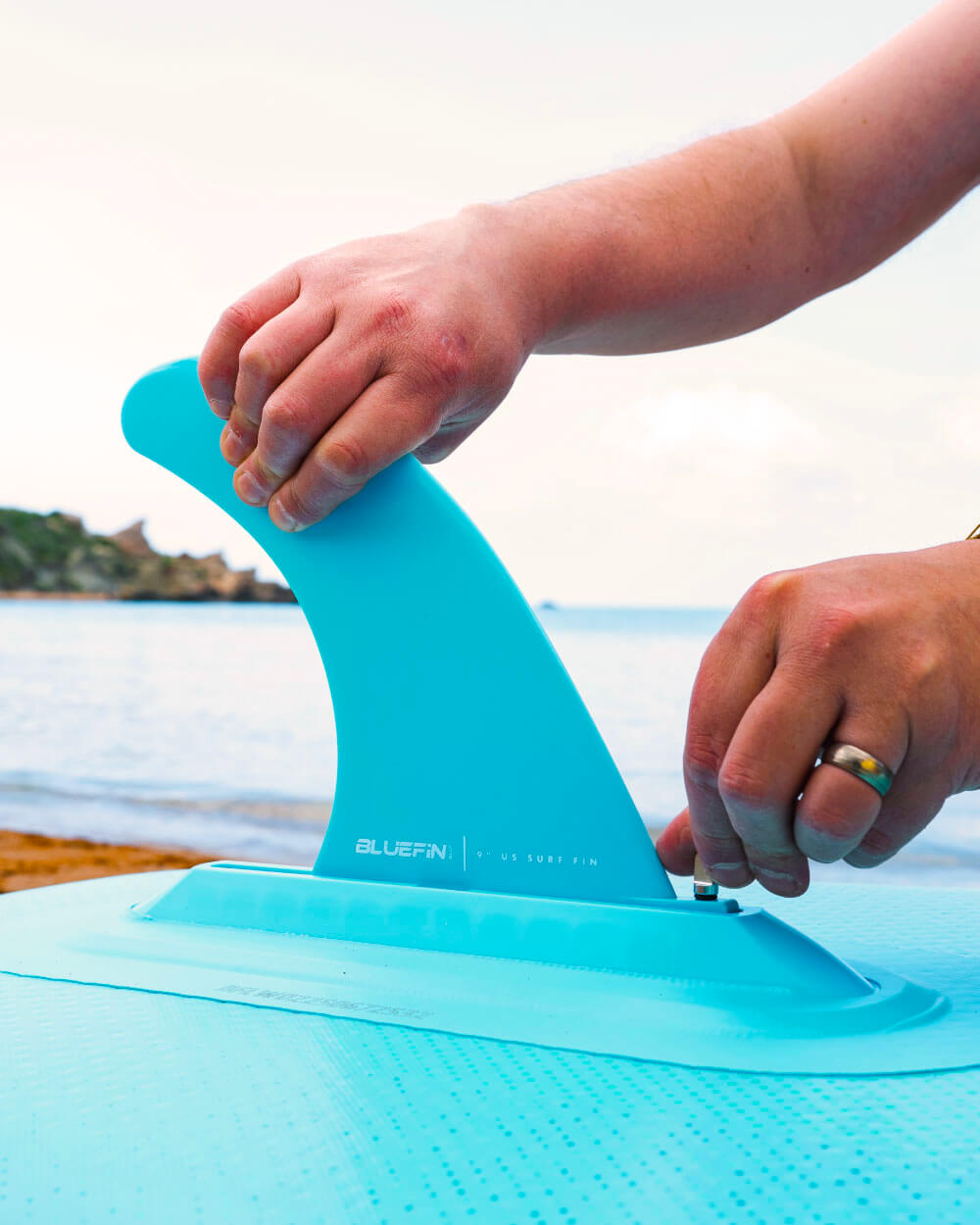 Up close shot of someone setting up the fin on a Bluefin Cruise 10'8 blue gecko Inflatable Paddle Board on the beach
