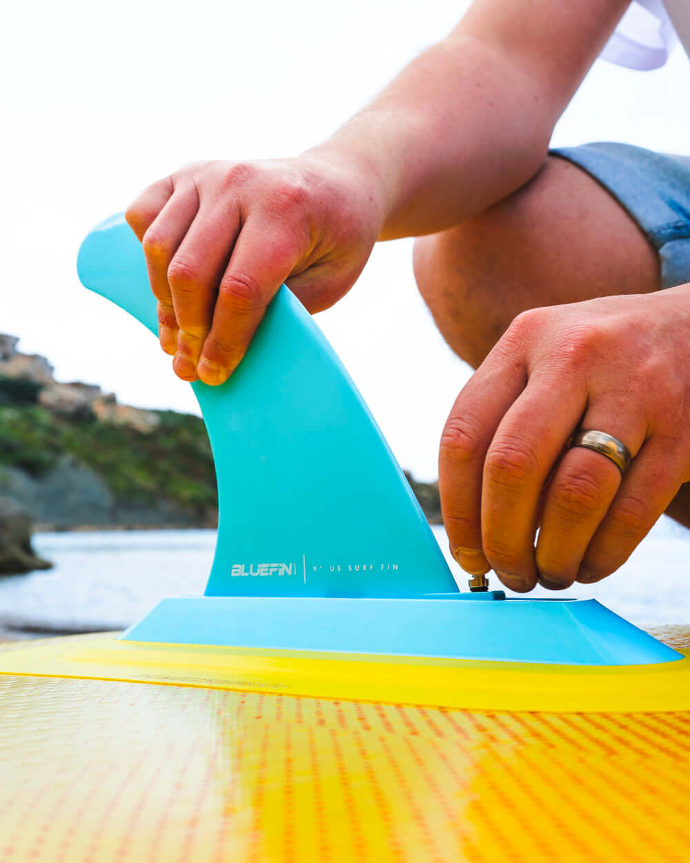 Up close shot of someone setting up the fin on a Bluefin Cruise 10'8 Orange Sunset Inflatable Paddle Board on the beach