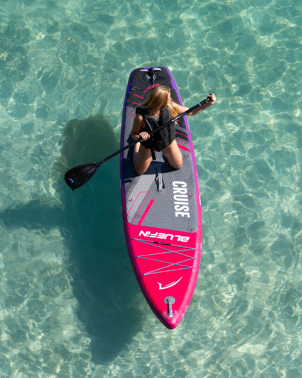 Paddleboarder on a vibrant inflatable SUP in clear water, enjoying a sunny day outdoors.