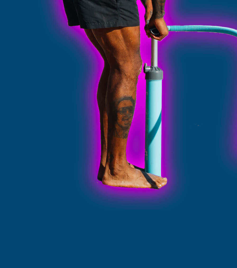 Person inflating a paddleboard with a blue pump on a vibrant background.