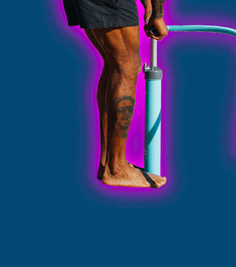 Person inflating a paddleboard with a blue pump on a vibrant background.