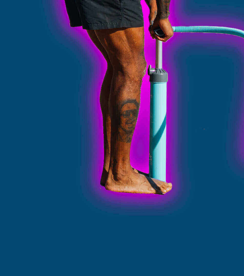 Person inflating a paddleboard with a blue pump on a vibrant background.