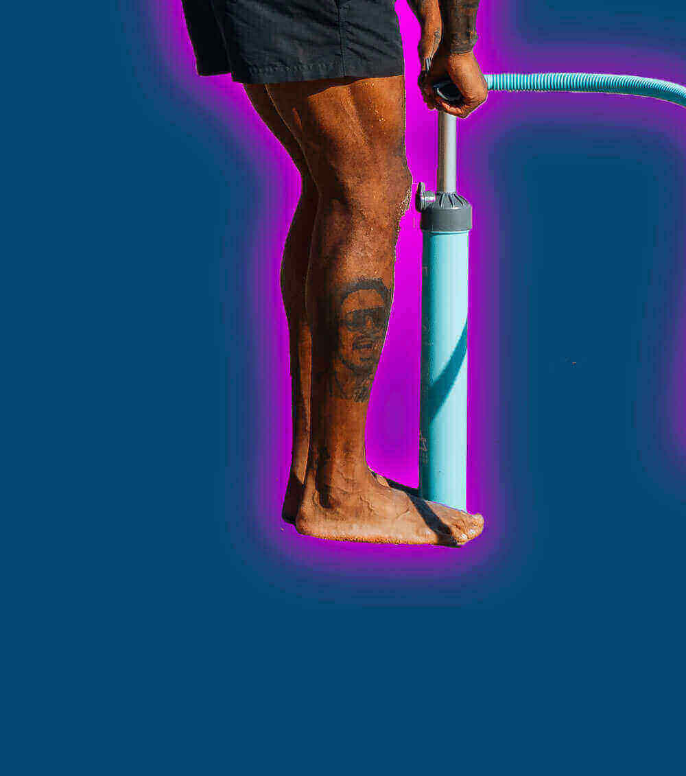 Person inflating a paddleboard with a blue pump on a vibrant background.