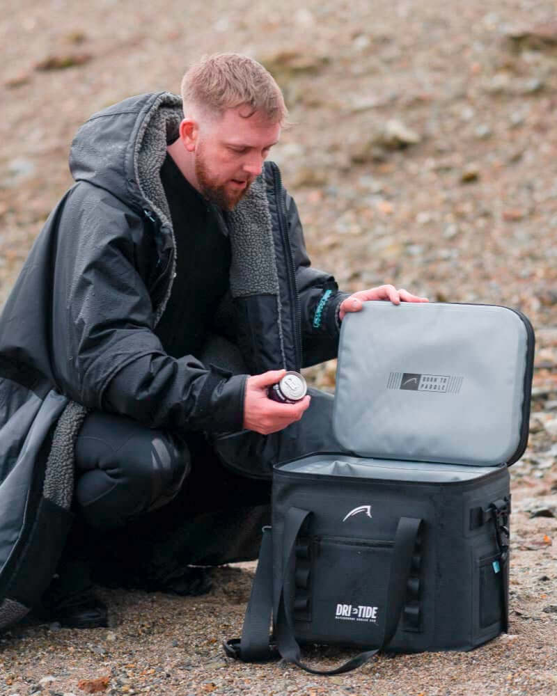Man in outdoor setting packing a black and gray Dri-tide cooler bag