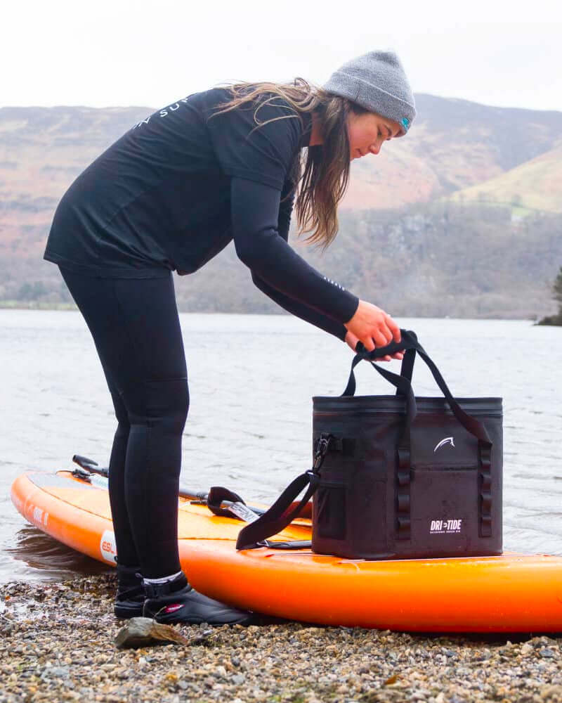 Person preparing for paddleboarding with an inflatable sup paddle board and a black Dri-Tide cooler bag on the deck