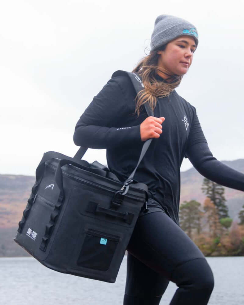 Person carrying a black Dri-Tide bag outdoors with a scenic background
