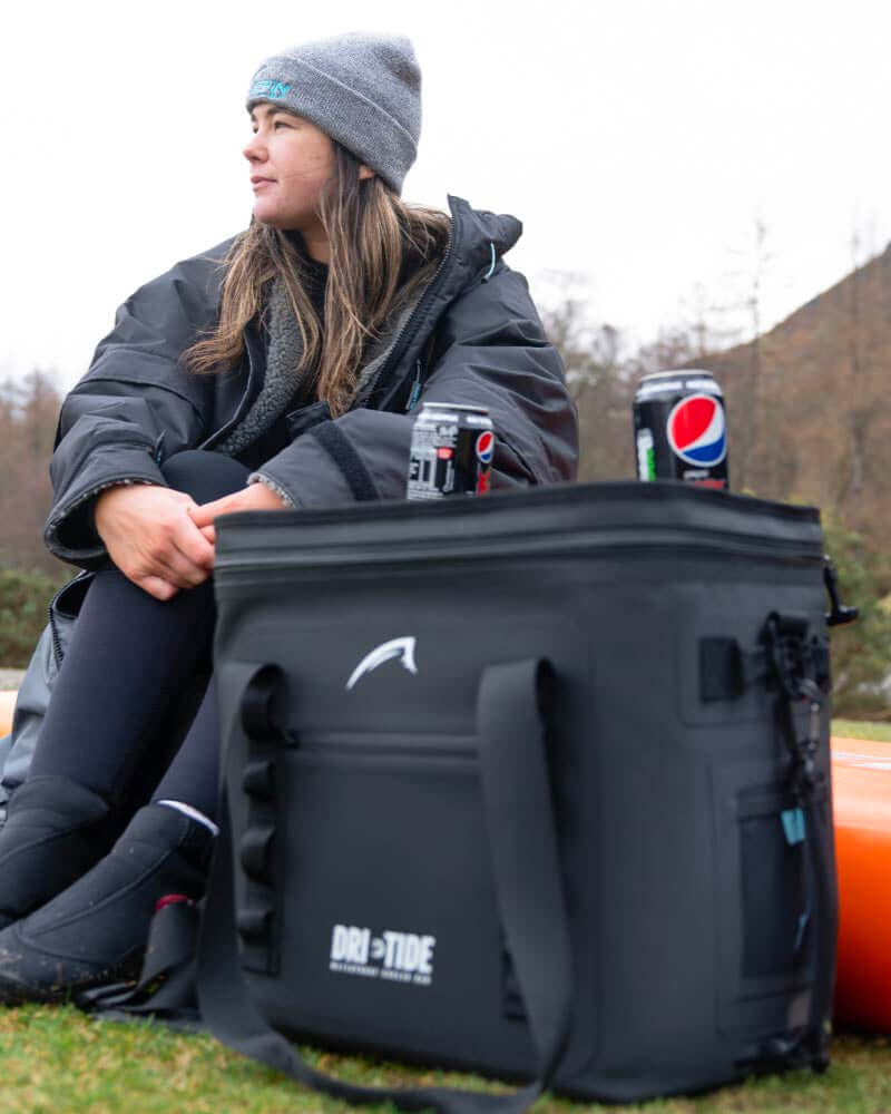 Person sitting outdoors with a black Dri-Tide cooler bag and pop cans