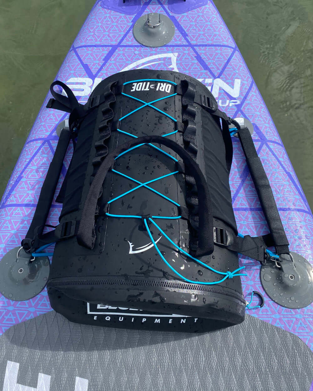 Black dri-tide backpack with blue bungee straps on a purple inflatable paddle board