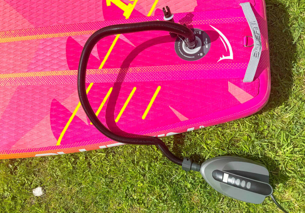 Electric pump connected to a pink inflatable SUP on green grass.