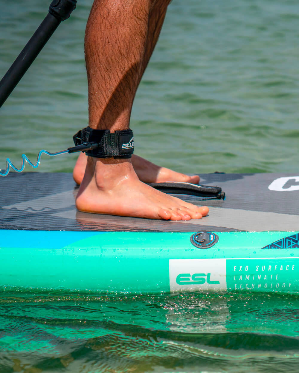 Person standing on a bluefin cruise in gecko blue stand-up paddleboard in water.