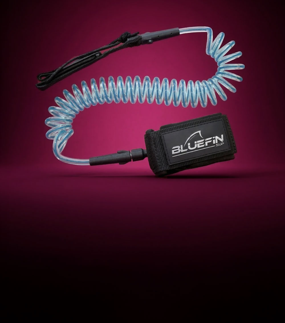 Coiled SUP leash with black ankle strap and blue elastic cord on a pink background