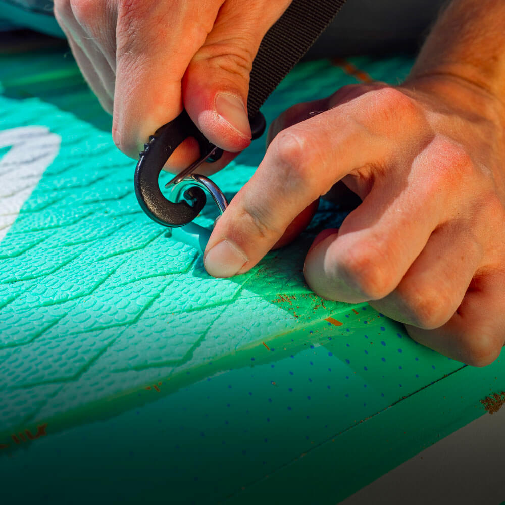 Person adjusting a strap on a textured turquoise paddleboard.