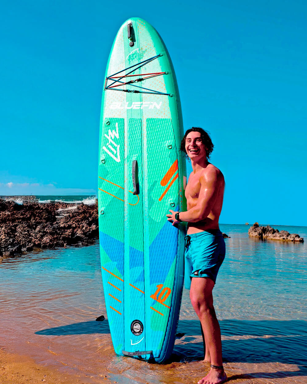Man on the beach holding up the Blue Lagoon 10' Lite Bluefin paddle board