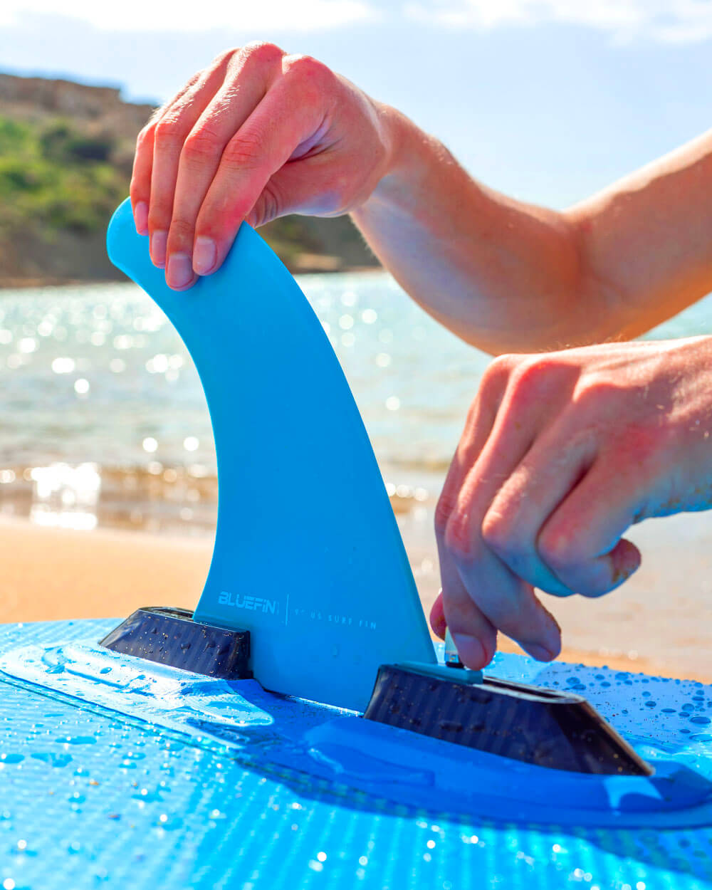 Up close shot of someone setting up the fin on a Bluefin Blue Lagoon 10' Lite inflatable paddle board on the beach