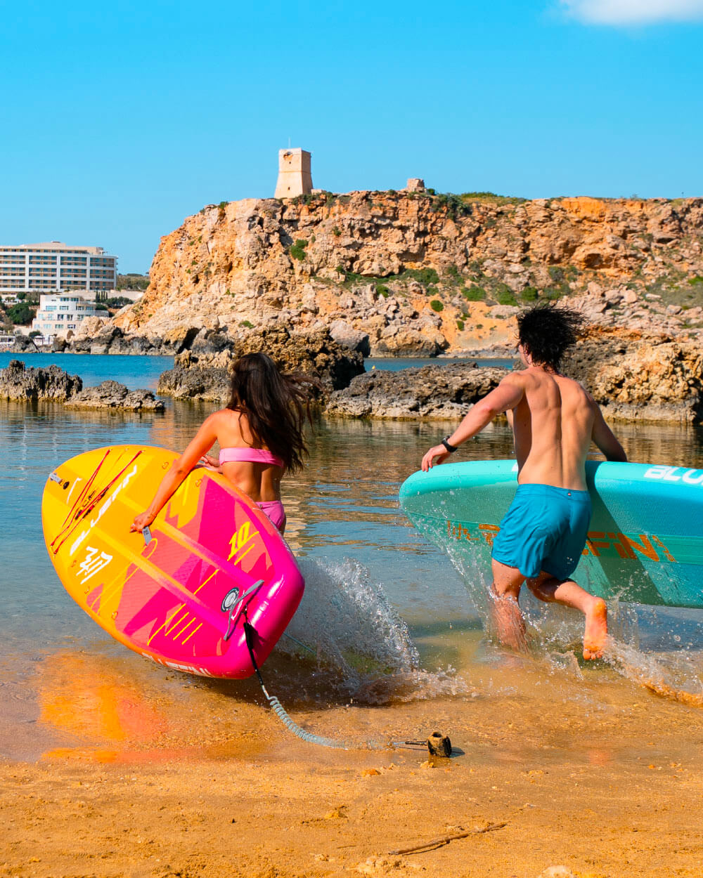 two people running towards the ocean carrying a Bluefin lite inflatable paddleboard each