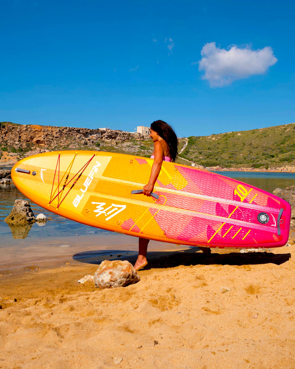 Woman walking on the beach holding a Pink Coral 10' Lite Bluefin sup paddle board