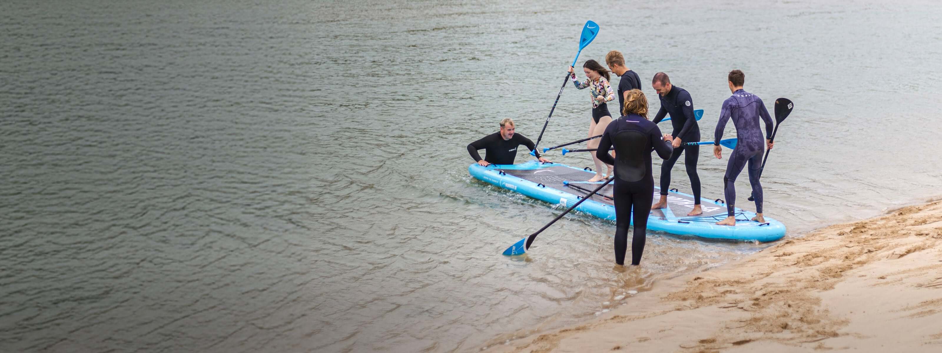 Group of people preparing to paddleboard on calm water, enjoying outdoor adventure together.