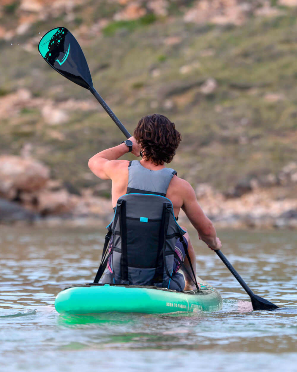 Person paddling on a green inflatable paddleboard with a black paddle, facing away from the camera.