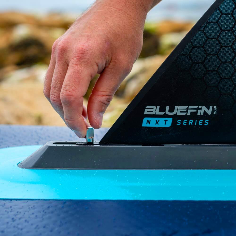 Hand adjusting the fin attachment on a Bluefin SUP NXT Series paddleboard.
